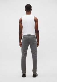 Pantalons gris à coupe slim, fabriqués en tissu mélangé coton. Caractérisés par des poches arrière et une texture lisse. Portés avec un haut sans manches blanc.