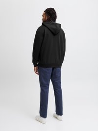 Μαύρη κουκούλα με χαλαρή εφαρμογή, συνδυασμένη με ναυτικά παντελόνια και λευκά αθλητικά παπούτσια. Το ύφασμα φαίνεται λείο και άνετο.