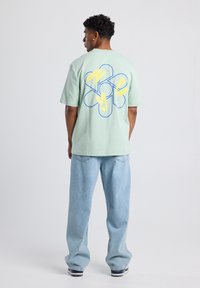 Light green cotton t-shirt featuring a blue and yellow flower graphic on the back. Paired with light blue baggy jeans.