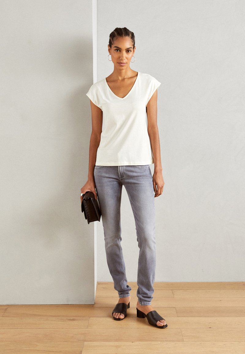 Witte V-hals T-shirt met kapmouwen, gecombineerd met lichtgrijze skinny jeans en zwarte hak-sandalen, met een gestructureerde zwarte handtas.