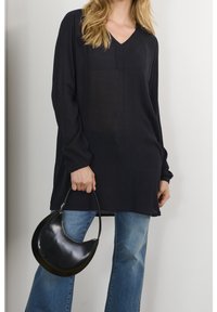 Blouse noire à manches longues avec un col en V et une coupe décontractée, associée à un jean évasé bleu clair et un sac à main noir en forme de croissant.