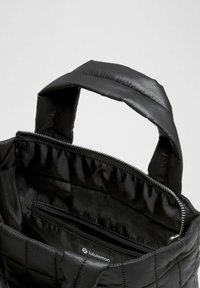 Schwarze gesteppte Stofftasche mit gepolsterten Trägern. Verfügt über einen Reißverschluss und eine Innentasche. Dezentes Logoschild im Inneren. Sanfte Textur.
