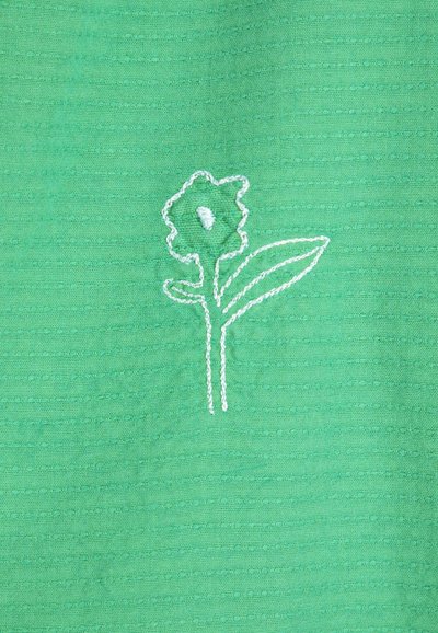 Tissu vert avec une simple fleur blanche brodée, comprenant une tige unique, deux feuilles et une fleur à cinq pétales avec un détail au centre.