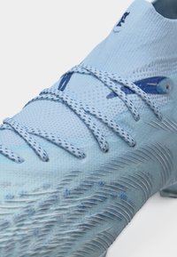 Αθλητικό παπούτσι σε ανοιχτό μπλε χρώμα με σόλα με υφή για καλύτερη πρόσφυση και κορδόνια με σχέδιο, που διαθέτει κολάρο αστραγάλου σε ύφασμα τύπου κάλτσας και διακριτικό λογότυπο.