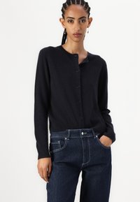 Navy cardigan made of soft material, featuring a round neckline, six buttons down the front, and long sleeves, paired with dark denim jeans.