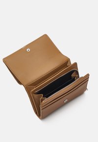 Portefeuille en cuir tan avec fermeture à bouton-pression, comprenant plusieurs emplacements pour cartes et des compartiments zippés. Finition texturée avec doublure intérieure noire.