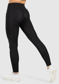 Zwarte hoge tailleleggings met een gladde textuur, een strakke pasvorm en een achterzak; gecombineerd met witte sportschoenen met een gestructureerde zool.