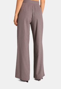 Pantalons larges violets avec des rayures verticales et des accents métalliques subtils. Tissu lisse avec une coupe ajustée et une taille large.