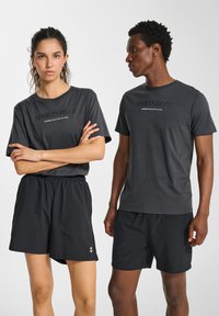Mörkgrå t-shirts med texten "SPORTS DEPT.", tillsammans med svarta shorts. Båda är gjorda av lätt, andningsbar tyg. Minimalistisk design.