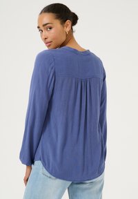 Blauwe blouse met lange mouwen van textuurstof, met een geplooid rugdetail en een ronde zoom. Gemaakt met lichtblauwe jeans.