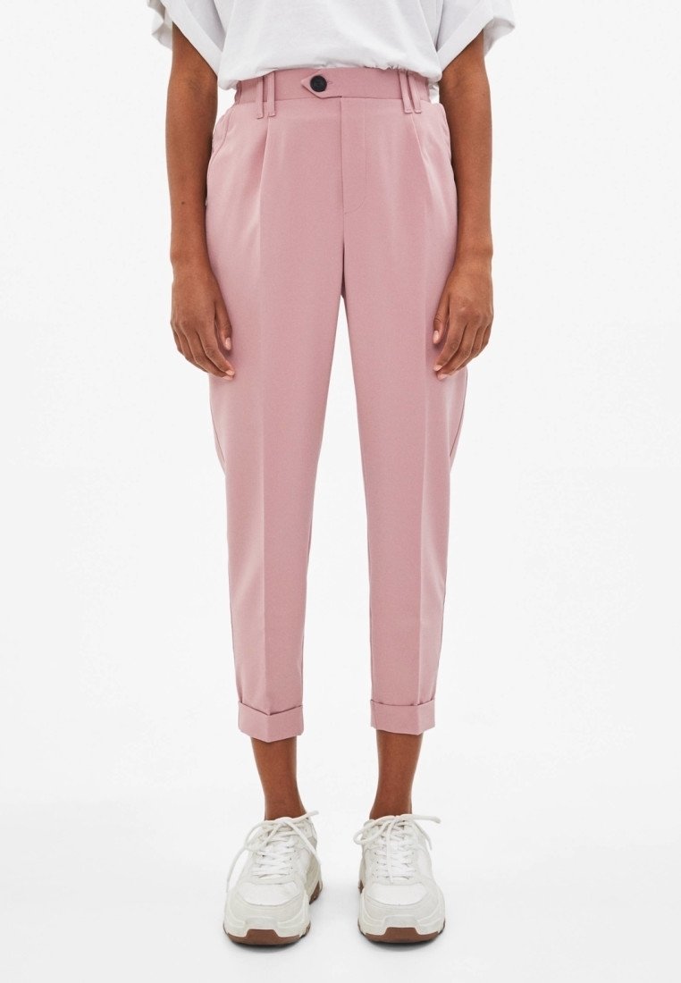 Personne portant un pantalon rose taille haute, court et sur mesure avec des ourlets retournés, associé à des baskets blanches épaisses et un top blanc rentré.