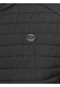 Sort polstret jakke med quiltet tekstur, gummilogo-patch med hvid tekst "JACK & JONES" og glat stof med en mat finish.