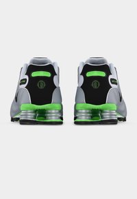 Αθλητικά παπούτσια Nike Shox σε γκρι και μαύρο με πράσινες λεπτομέρειες. Διαθέτουν μαλακή σόλα, λείο υφή και εμφανή στοιχεία απορρόφησης κραδασμών.