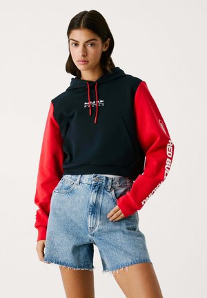 Svart huvtröja med röda ärmar, med en framficka och Red Bull Racing-logotyp. Tillsammans med ljusblå denimshorts med fransar.