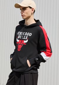 Felpa nera con il testo "CHICAGO BULLS" e una grafica di un toro rosso. Presenta accenti rossi, bianchi e neri sulle maniche, tasca a canguro e cappuccio con coulisse.
