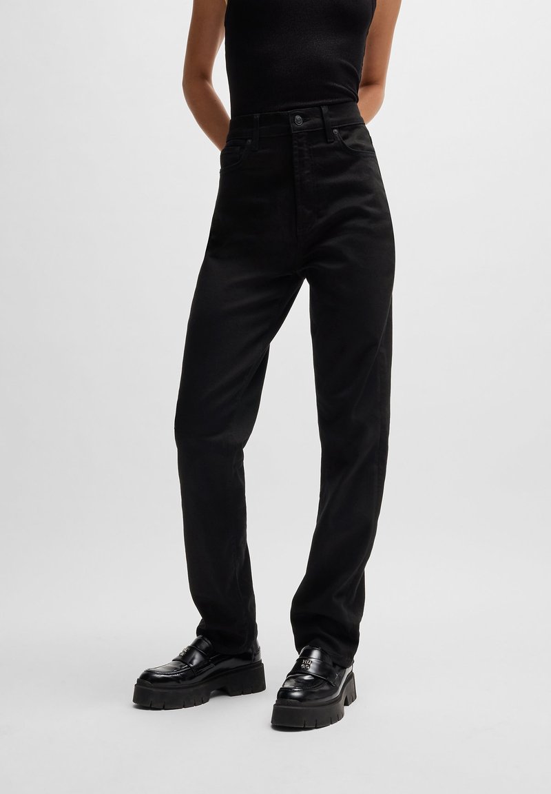 Pantalon noir taille haute en mélange de coton, avec jambes droites, poches avant et fermeture à boutons. Associé à des chaussures plateformes noires.