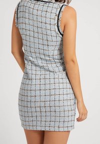 Robe sans manches en tissu tissé bleu clair à carreaux, avec des bords effilochés et une silhouette ajustée.