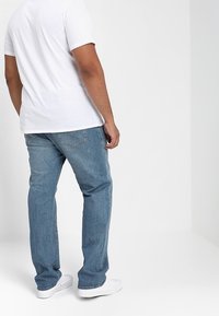 Jeans in denim azzurro chiaro con un taglio rilassato, dotati di tasche posteriori e orlo sfrangiato, abbinati a una t-shirt di cotone bianca semplice.