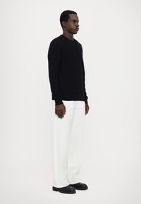 Pull en maille bleu marine avec un motif en losanges, associé à un pantalon large blanc et des bottes noires à lacets, présenté de côté.