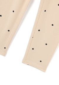 Beige leggings van zacht stof met een patroon van zwarte stippen. De boorden zijn netjes gestikt, wat het ontwerp benadrukt.