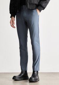 Maßgeschneiderte blaue Hosen aus glattem Stoff, schlanker Schnitt, mit Seitentaschen und einem Knopfverschluss, kombiniert mit schwarzen Stiefeletten.