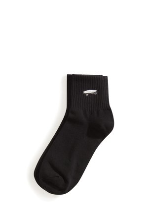 Paire de chaussettes noires chevilles avec des bords côtelés et une petite icône blanche de skateboard sur le dessus.