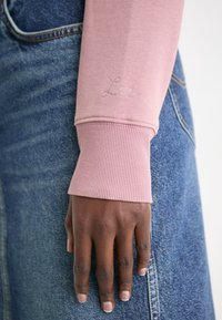 Różowa, długosleeve'owa koszula z ribbowymi mankietami, z subtelnym wyhaftowanym logo "Lee", zestawiona z niebieską spódnicą dżinsową z widocznymi detalami kieszeni.