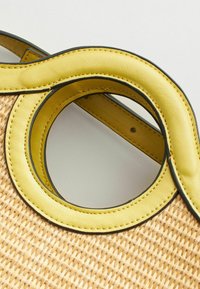 Sac en paille tissé avec une poignée en cuir jaune arrondie et des bordures noires, présentant une surface texturée et un design de poignée circulaire.