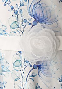 Biała sukienka w niebieski kwiatowy wzór z wytłoczonymi kropkami. Posiada biały akcent w postaci materiałowego kwiatu oraz gładki, biały pasek w talii.