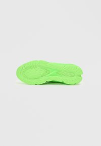 Grüne Gummisohle eines Sneakers mit strukturiertem Muster für besseren Halt, breiter Ferse und abgerundetem Zehenbereich für Stabilität.