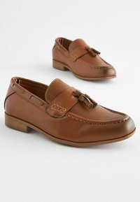Mocassins en cuir marron avec un devant texturé, des glands décoratifs, des coutures contrastantes et un petit talon en bois.