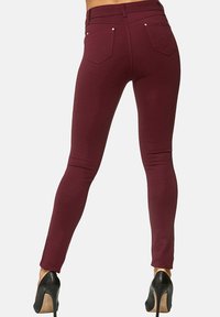Leggings bordeaux realizzati in tessuto elasticizzato, con vita alta, design aderente e due tasche posteriori con dettagli argentati.