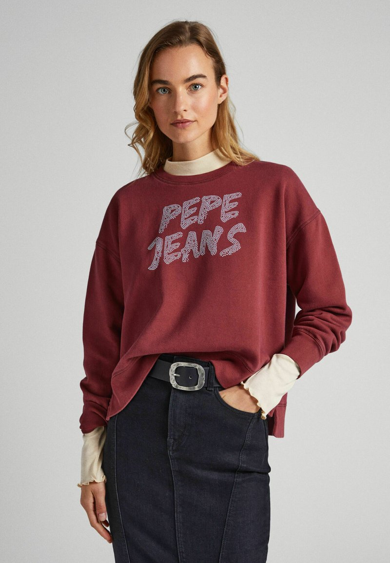 Sweatshirt bordeaux con la scritta "PEPE JEANS" in strass argentati. Presenta una vestibilità comoda, colletto rotondo e polsini a coste sopra una maglietta a maniche lunghe color crema.