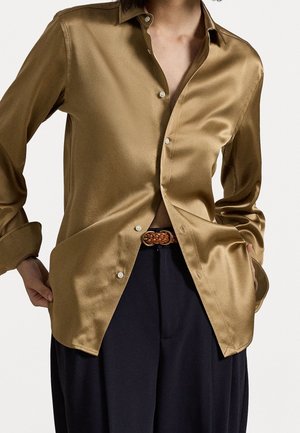 Satijnen bruine overhemd met knopen en een kraag, slim fit, lange mouwen en witte knopen. Gecombineerd met zwarte broek en een gevlochten riem.