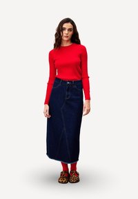 Pull en maille côtelée rouge, jupe maxi en denim taille haute avec détail sur les coutures latérales, et des chaussures imprimé léopard. Les textures des tissus varient.