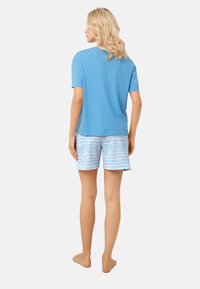 Jasnoniebieska bawełniana koszulka z krótkim rękawem, w zestawieniu z białymi szortami z niebieskimi paskami. Model pokazany z tyłu, boso.