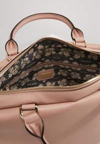 Ljusrosa läderhandväska med en texturerad yta, guldfärgad detaljering och ett mönstrat svart inre med små blommönster. Fick sluten med dragkedja inuti.