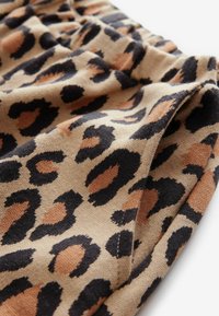 Tissu à imprimé léopard en beige, avec des taches noires et brunes. Texture douce avec un élastique froncé à la taille.