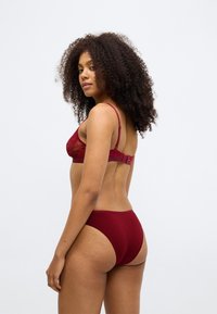 Burgundowa koronkowa biustonosz z regulowanymi ramiączkami i zapięciem na haczyk, zestawiona z pasującymi majtkami typu high-waisted, charakteryzuje się gładką fakturą i bezszwowym designem.