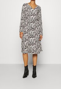 Svart blommig klänning med långa ärmar, V-ringning och midjeband. Har rosa och vita blommor, knä-lång fåll och är matchad med svarta ankelstövlar.