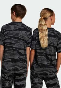 Camisas de camuflaje negras de manga corta con diferentes tonos de gris, que presentan un corte relajado y una textura de tela suave, visibles desde la parte trasera.