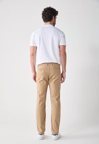 Pantaloni kaki leggeri con design a gamba dritta, in tessuto di cotone, due tasche posteriori e cintura, abbinati a una maglietta bianca semplice.