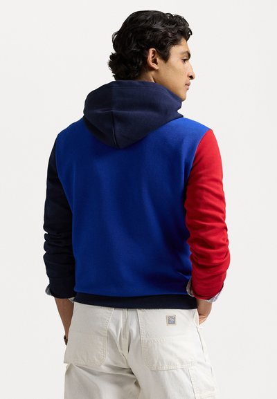 Hooded sweatshirt with a blue body, navy sleeves, and red accents. Cotton blend fabric with ribbed cuff and hem. Relaxed fit.