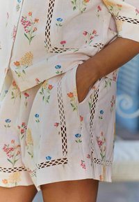 Floral-patterned linen garment featuring a light pink base, decorative lace cutouts, and side pockets for added functionality.