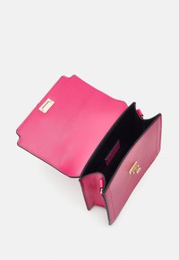 Rosa läderhandväska med svart kant, med en slät yta, guldspänne och en öppen insida utan ytterligare fack.