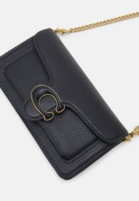 Billetera de piel negra con un acabado texturizado, que cuenta con una cadena en tono dorado, un acento distintivo en el cierre y una forma rectangular compacta.
