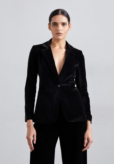 Sorte fløjl blazer med dyb V-udskæring, enkelt knaplukning, skræddersyet pasform og glatte revers, parret med matchende sorte bukser.