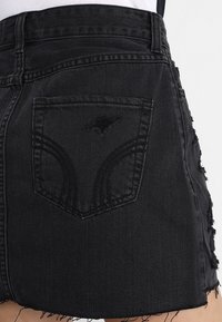 Černá džínsová sukně s třepeným lemem, opotřebovanou strukturou a zadní kapsou s jemným prošíváním.