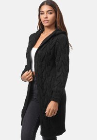 Cardigan nero in maglia con cappuccio, caratterizzato da un motivo a trecce e maniche lunghe. Design aperto sul frontale, di lunghezza al ginocchio, in tessuto testurizzato.