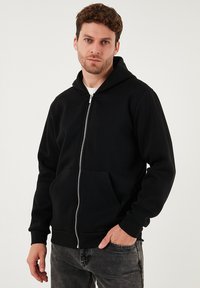 Černá mikina na zip s přední kapsou, s podšitou kapucí a kontrastním zipem. Vyrobená z měkké látky se standardním střihem.